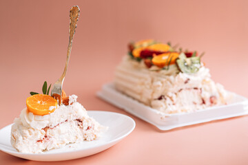 Festive meringue roll cut on round plate with fork on pink background.