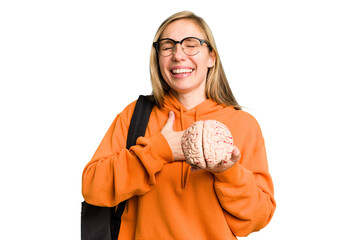 Young student caucasian woman holding a brain isolated laughs out loudly keeping hand on chest.