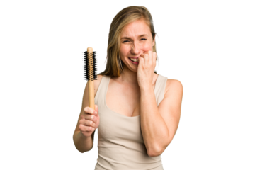 Young caucasian woman using an hair comb isolated biting fingernails, nervous and very anxious.