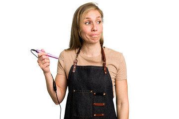 Young caucasian manicurist woman holding an electric file drill isolated confused, feels doubtful and unsure.