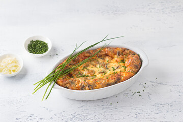 Casserole or clafoutis with mushrooms and cheese in a white ceramic baking dish sprinkled with green onions on a light background. Delicious homemade food