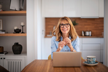 Attractive woman with laptop sitting in the dining room and working at home