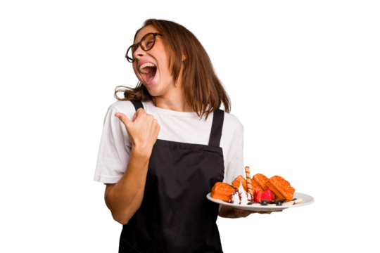 Young caucasian woman holding a waffles dish isolated points with thumb finger away, laughing and carefree.