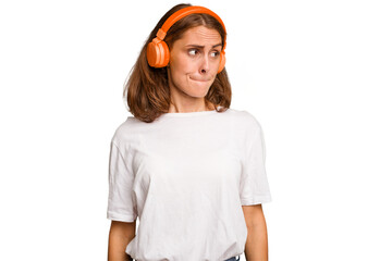 Young caucasian woman listening to music with headphones isolated confused, feels doubtful and unsure.