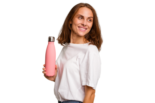 Young caucasian woman holding a pink thermo isolated looks aside smiling, cheerful and pleasant.