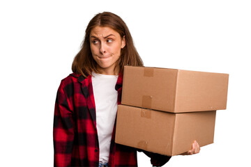 Young caucasian woman moving while picking up a box full of things isolated confused, feels doubtful and unsure.