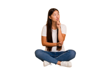 Young asian woman sitting on the floor cutout isolated looking sideways with doubtful and skeptical expression.