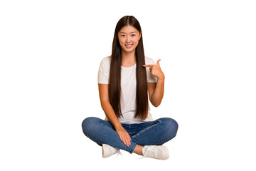 Young asian woman sitting on the floor cutout isolated person pointing by hand to a shirt copy space, proud and confident