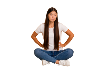 Young asian woman sitting on the floor cutout isolated confused, feels doubtful and unsure.