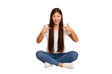 Young asian woman sitting on the floor cutout isolated surprised pointing with finger, smiling...