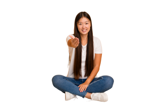 Young asian woman sitting on the floor cutout isolated stretching hand at camera in greeting gesture.