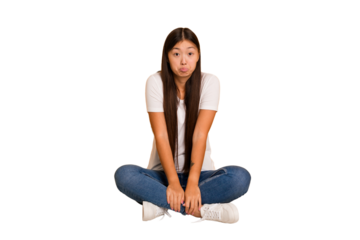 Young asian woman sitting on the floor cutout isolated shrugs shoulders and open eyes confused.