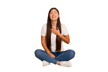 Young asian woman sitting on the floor cutout isolated laughs out loudly keeping hand on chest.