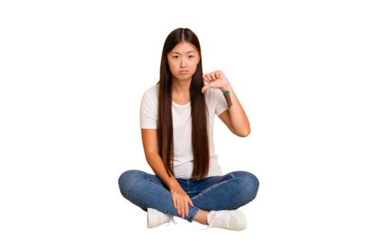 Young asian woman sitting on the floor cutout isolated showing a dislike gesture, thumbs down. Disagreement concept.