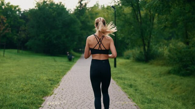 Back view of the female athlete is running in the park wearing black sportswear. Following shot active female runner. Sport people concept.