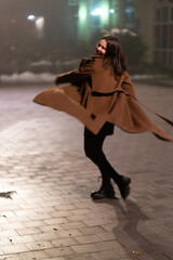 young woman in a coat dancing in a night foggy city