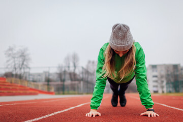 Young woman in sportswear doing plank or push ups outdoors on winter sportsground. Workout on...