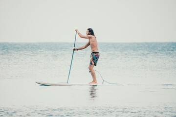 Sea man sup. Asian athlete man swimming in sea and paddleboarding at summer sunset. Healthy strong male enjoy outdoor active lifestyle and water sports on holiday vacation. Slow motion