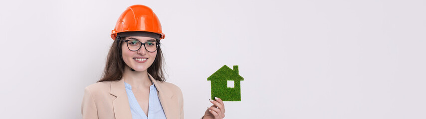 A girl in a construction helmet holds a green house. The concept of ecological clean housing.