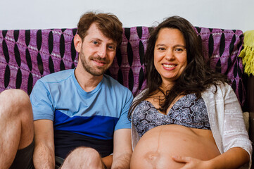 portrait of argentinian man with his brazilian pregnant wife sitting smiling, looking at the camera.