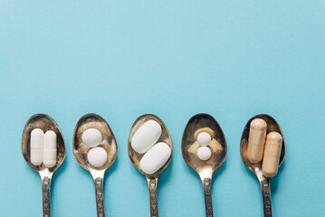 Different tablets and capsules in teaspoons on a pastel background. Tablets and pills.