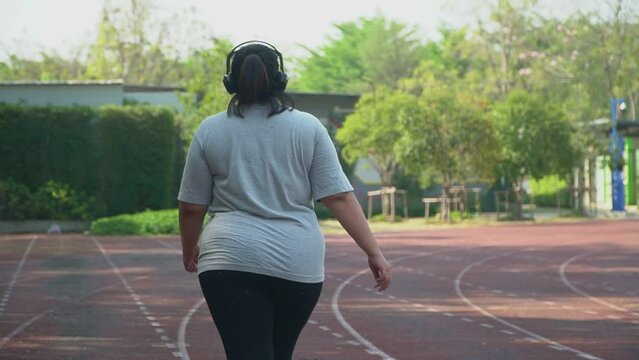 Happy overweight Asian women Wearing headphones to music and Walking on the treadmill of the stadium. Concept of Health care And weight loss through exercise  - shot in slow motion.