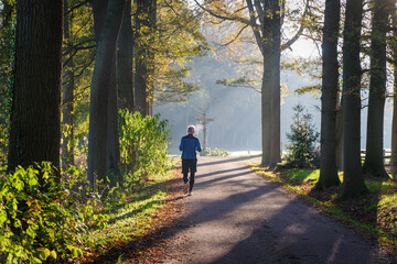 Obraz premium OLDENZAAL, NETHERLANDS - NOVEMBER 20, 2022: Senior jogger running on a sunny autumn day in a beautiful natural surroundings.