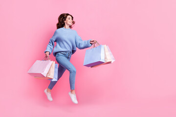 Full body profile portrait of overjoyed cheerful lady hold packages jump rush empty space isolated on pink color background