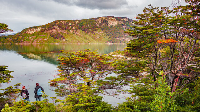Two hikers standing at the Ensenada Zaratiegui Bay in austral subpolar forest in Tierra del Fuego National Park, near Ushuaia and Beagle Channel, Patagonia, Argentina, in Autumn colors.