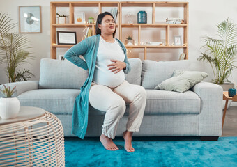 Pregnant woman, discomfort and back pain sitting on the living room sofa and holding tummy at home....
