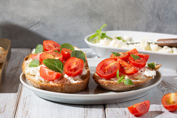 Sandwich with cottage cheese, tomatoes and basil on white wooden background. Traditional Italian bruschetta. Healthy savory feta and tomato toast. Close-up.