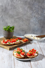Sandwich with cottage cheese, tomatoes and basil on white wooden background. Traditional Italian bruschetta. Healthy savory feta and tomato toast. Copy space.