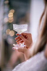 The hands of a woman hold a glass of champagne on a background of golden beke. The concept of the holiday, Christmas, new year, birthday.