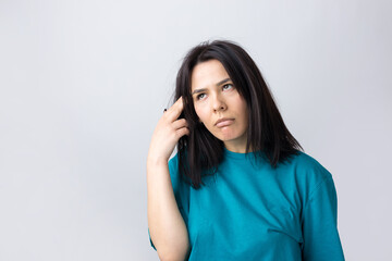 Portrait of a beautiful girl in a blue t-shirt, looks aside with pensive expression, is considering a plan for further action.