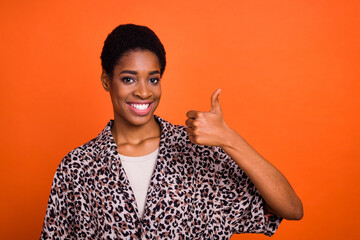 Portrait of attractive cheerful trendy girl with short hair showing thumbup isolated over bright orange color background