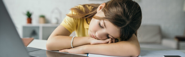 Obraz na płótnie Canvas tired schoolgirl sleeping near blurred laptop at home, banner