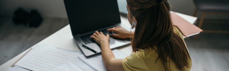 back view of girl typing on laptop with blank screen while studying at home, banner