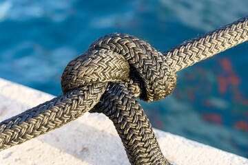 Nautical knot on a yacht rope against the background of water on the pier. Yacht tied with a rope...