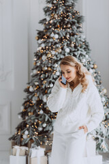 happy european businesswoman talking on mobile phone with client at workplace with decorated Christmas tree behind, smiling woman working in home office during winter holidays. Soft selective focus.