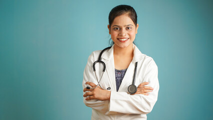 Portrait of a young female doctor wearing apron and stethoscope, Cheerful Asian Indian woman doctor isolated over blue studio background