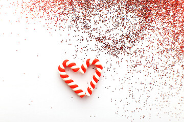Christmas composition with candy canes in form oh heart on blue wooden background with red sequins