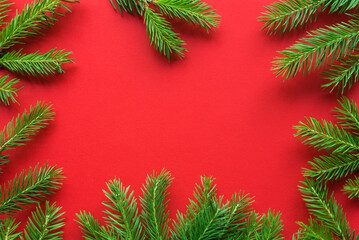 Fototapeta na wymiar Christmas frame made of Christmas tree branches with bokeh lights on a plain paper red background, copy space