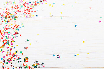 Christmas background with candy canes and multicolored sequins on blue wooden background