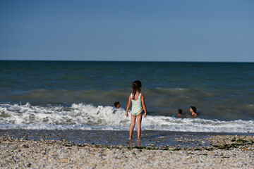 Back of baby girl looking on her family swimming at sea in beach Porto Sant Elpidio, Italy.