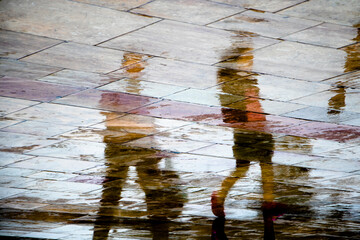 Abstract blurry silhouette reflections of unrecognizable people walking on wet city street pavement on a rainy day - 552052733