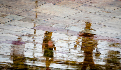 Abstract blurry silhouette reflections of unrecognizable people walking on wet city street pavement on a rainy day - 552052735