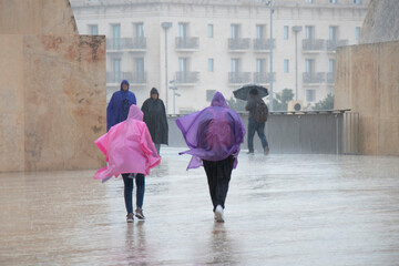 People wearing rain ponchos and umbrellas walking on a rainy day in Valletta, Malta