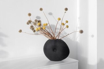 Minimalist composition of dried round flowers on a long stems in shape ceramic vase as home decoration.