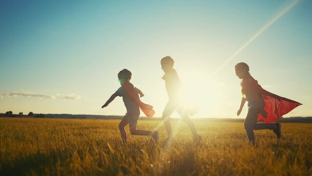 team superhero. a group of children are running across the field in a superhero costume with a silhouette of a red cape at dream sunset. the concept of a happy family childhood. teamwork superhero