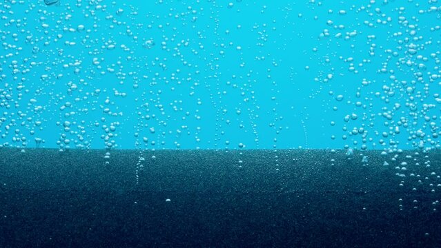 Small shiny air bubbles escaping from grey paralon compressor tube or filter under water. Macro shot of working equipment for aeration of water with oxygen in aquarium on blue background. Slow motion.